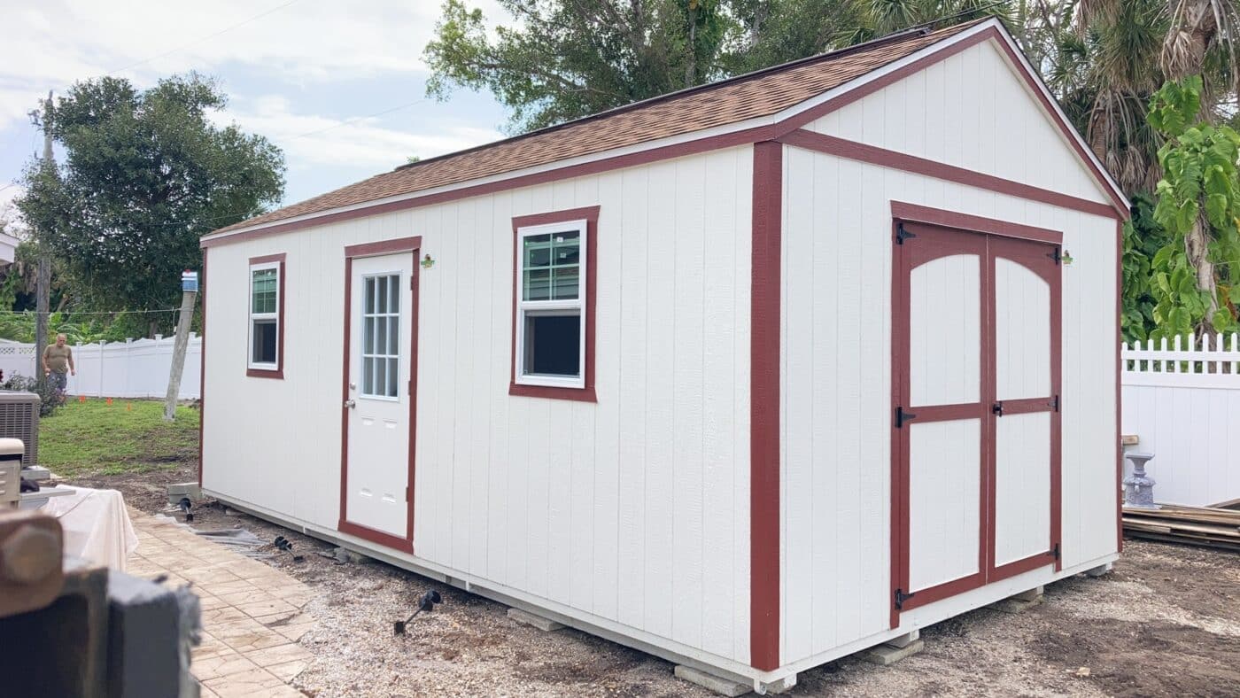 white shed with red trim, a double door, a standard door on the side, and two windows