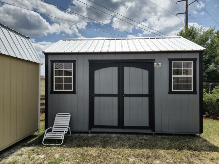 a grey side gable shed with black trim, two windows, and double doors, standing near another shed in venus fl